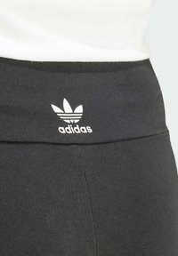 Leggings sportivi neri con una texture liscia e una fascia in vita ampia, caratterizzati da un logo Adidas bianco e un design a tre strisce.