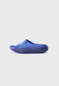 Sandale en slide Nike bleue avec une semelle épaisse et rainurée et un dessus lisse, présentée sur un fond blanc, vue de côté droit.