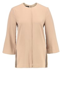 Veste beige à manches longues pour femmes avec encolure ronde, fermeture éclair frontale et fentes latérales, en tissu lisse.