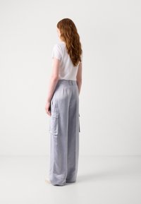 Lichtgrijze cargobroek met een gladde textuur, voorzien van zijzakken en een relaxed fit, gecombineerd met een eenvoudig wit T-shirt.