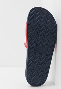Kék gumi papucs talp zigzag mintával, piros pánttal és texturált tapadással. A talpon a "Levi's" márkájú logó van gravírozva.