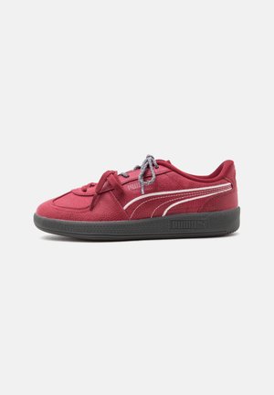 Κόκκινο αθλητικό παπούτσι Puma με μαύρη σόλα, λευκή πλευρική ρίγα, υφή υλικού και γκρι κορδόνια σε απλό λευκό φόντο.