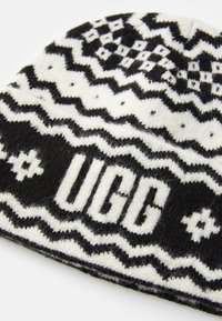 Czarna i biała czapka dzianinowa z geometrycznym wzorem oraz wyraźnie wyeksponowanym słowem "UGG" w pogrubionych literach. Miękka tekstura.