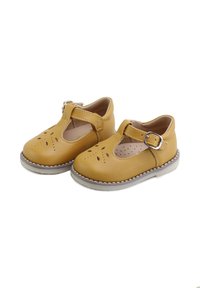 Par de zapatos tipo Mary Jane para niños pequeños en color mostaza, con tiras de hebilla, recortes florales perforados y suelas de goma grises sobre un fondo blanco.