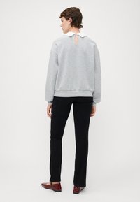 Grauer Pullover mit weißem Kragen, ausgestattet mit einem Schlüsselloch-Detail im Rücken. Kombiniert mit schwarzen Schlaghosen und roten Lackschuhen.