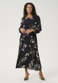 Melna plisēta kleita ar garām piedurknēm, ziedu raksts baltā un brūnā krāsā, apaļa izgriezuma, viegla auduma, apvienota ar bēša augstiem papēžiem.