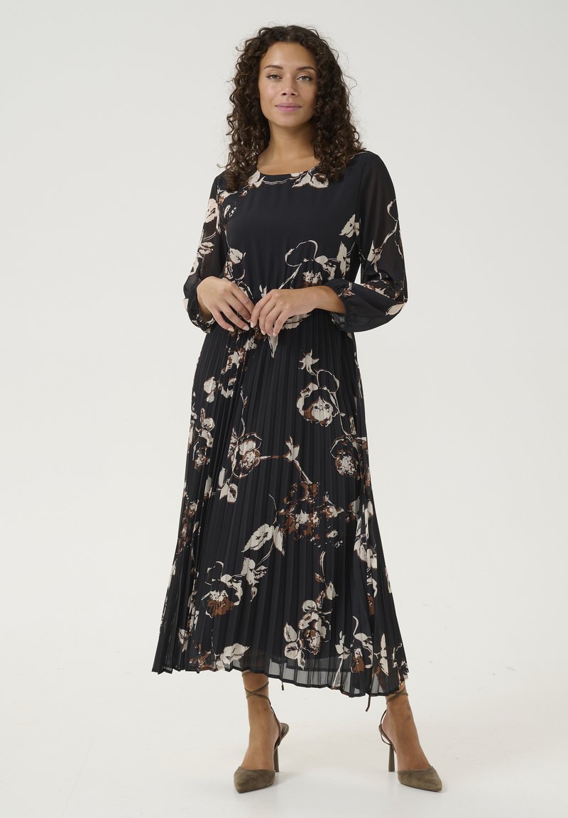 Melna plisēta kleita ar garām piedurknēm, ziedu raksts baltā un brūnā krāsā, apaļa izgriezuma, viegla auduma, apvienota ar bēša augstiem papēžiem.