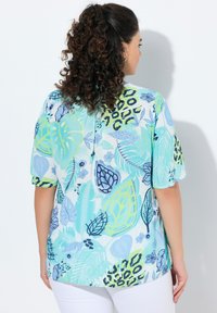 Blusa a maniche corte con sfondo azzurro chiaro, caratterizzata da una vivace stampa di foglie e animali in tonalità di verde e blu scuro, realizzata in un tessuto morbido.