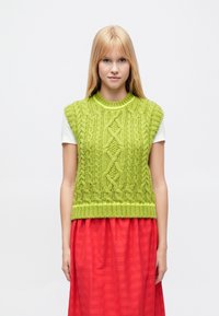 Laimiņzaļš adīts džemperis bez piedurknēm ar teksturētiem pinuma rakstiem, ribainu apakšmalu un īsām piedurknēm, komplektā ar plūstošu sarkanu svārku.