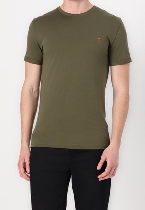 Homme portant un t-shirt ajusté vert olive à manches courtes avec un petit logo orange "II" sur le côté gauche de la poitrine, associé à un pantalon noir.