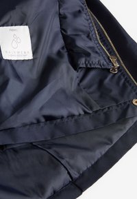 Marine vandtæt regnjakke med letvægtsstof, med en guldfarvet lynlås og indvendig lomme. Etiketten siger "next RAINWEAR SHOWER RESISTANT."