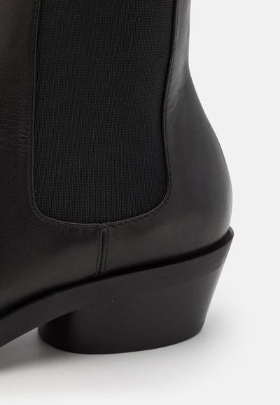 Botín de cuero negro con paneles laterales elásticos, un tacón curvado y un acabado suave para una apariencia elegante.