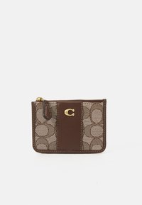 Ce porte-cartes en cuir brun et en mesh présente un motif géométrique, un logo doré et une fermeture à glissière pour un stockage sécurisé. Design compact.