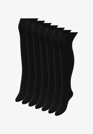 Hét pár fekete, átlátszatlan harisnyanadrág egymás mellett, lábtól derékig bemutatva.