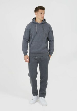 Hoodie gris avec cordons de serrage et poche avant, associé à un pantalon de survêtement assorti. Texture lisse, porté avec des baskets blanches.