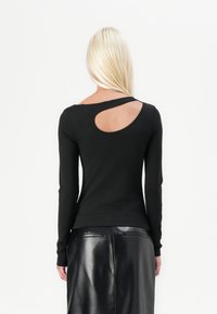 Schwarzes Langarmoberteil mit runder Rückenöffnung, figurbetontem Design und weicher Textur. Kombiniert mit einem Rock aus schwarzem Kunstleder.