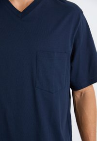 Granatowa koszulka V-neck wykonana z miękkiego materiału, z kieszonką na lewej piersi, krótkimi rękawami i luźnym fasonem. Gładka tekstura.