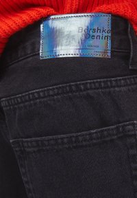 Los jeans de mezclilla negra presentan un diseño clásico con costuras visibles, un bolsillo trasero y una etiqueta reflectante azul que dice "Bershka Denim."