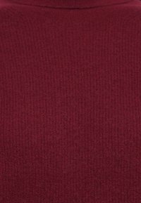 Pogled od blizu na maroon, fino pleteni rebrasti tkanino z visokim okruglim izrezom.