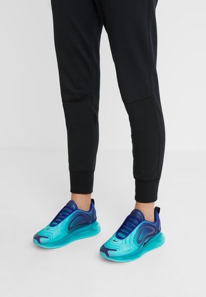 Baskets de sport dans des teintes de bleu et de turquoise, arborant un motif de vague et une semelle amortissante avec un talon prononcé et des détails texturés.