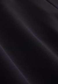 Close-up van glad, zwart stof met subtiele diagonale plooien en fijne textuur, die de zachte en matte materiaalkwaliteit benadrukt.