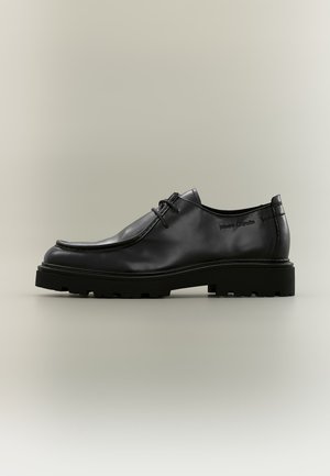Schwarzer Leder-Schnürschuh mit dicker profilierter Sohle und sichtbaren Nähten auf neutralem Hintergrund.