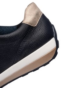 Detailní záběr paty černé texturované kožené tenisky s béžovým semišovým límcem a bílou a béžovou gumovou podrážkou.