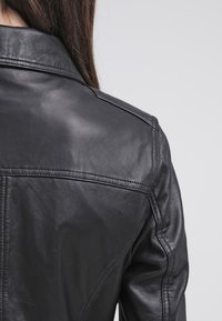 Black leather jacket featuring a smooth texture, pointed collar, and visible stitching details on the back.