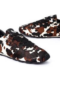 Zapatillas de piel de vaca con estampado de manchas en marrón y blanco, con cordones negros y suela texturizada, sutiles acentos en negro y costuras detalladas.