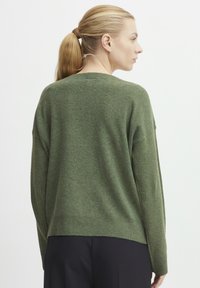Übergroßer grüner Strickpullover mit strukturiertem Finish, rundem Ausschnitt und geripptem Saum. Die Rückseite hat eine lockere Passform und abgesenkte Schultern.