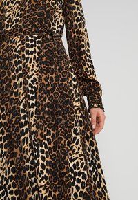 Abito con stampa leopardata in tonalità di marrone e nero, con maniche lunghe e vita cintrata. Presenta un tessuto morbido e fluido e polsini arricciati.