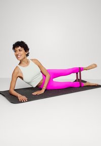 Conjunto de treino com um top cropped verde claro e leggings rosa brilhante. As leggings têm uma faixa escura que segura as pernas, utilizadas sobre um tapete preto com manchas.