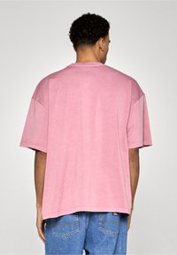 Růžové tričko s krátkými rukávy, volnějšího střihu, vyrobené z bavlny a s kulatým výstřihem. Na zádech jsou minimální šicí detaily.