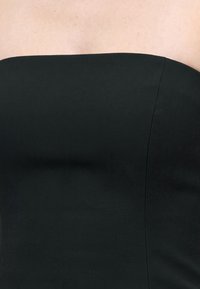 Gros plan sur des épaules nues et le haut de la poitrine portant un vêtement noir sans bretelles avec une texture de tissu visible et une ligne de couture.