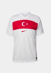 Maillot de football blanc avec une bande horizontale rouge ornée du drapeau de la Turquie et du logo Nike. Fabriqué en tissu respirant avec un col classique.