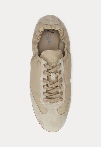 Sapatilha bege com uma combinação de texturas lisas e camurça, apresentando atacadores redondos e um colarinho acolchoado, com um logotipo na lingueta.