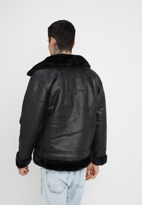 Chaqueta de cuero negra con un cuello y puños de piel sintética. El diseño presenta un acabado texturizado y una forma más corta y ajustada.