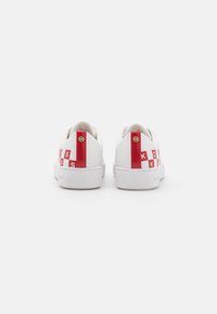 Baskets en cuir blanc avec des accents rouges sur le talon et les côtés, affichant une lettering de marque et une semelle plate en caoutchouc blanc.
