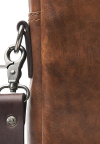 Detail einer braunen Ledertasche mit einem silbernen Metallschnapphaken und einem dunklen Ledergriff. Die Textur ist glatt mit subtilen natürlichen Variationen.