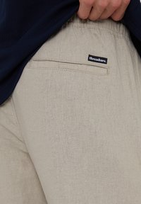Hellbeige Hosen aus einem strukturierten Stoff, mit einer Gesäßtasche und einem schwarzen Etikett mit "threadbare" sichtbar in der Nähe der Taille.