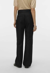Črne široke hlače z gladko teksturo, visokim pasom in zadnjimi žepi, v kombinaciji z lahkotnim bež zgornjim delom.