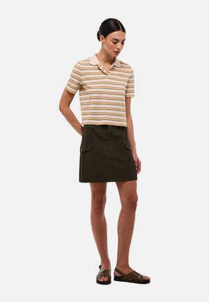 Polo à manches courtes à rayures beige et orange, associé à une jupe cargo verte foncée avec des poches latérales et des détails en boutons.