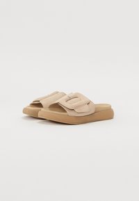 Beige suede slide sandals with a wide, textured strap featuring a silver buckle accent and a light brown rubber sole.