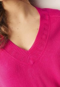 Pink v-neck sweater featuring ribbed collar and body texture, made of soft, lightweight material with a smooth finish.