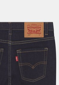 Jeans de mezclilla oscura con una etiqueta de cuero marrón que lleva "Levi Strauss & Co." y un logo rojo. El bolsillo trasero tiene un diseño bordado.