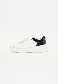 Valkoinen sneaker, jossa on mustia patenttikorostuksia, sileä pinta, pyöristetty kärki, hopeiset nauhakohdat ja valkoinen platform-pohja. Yksinkertainen, moderni muotoilu.