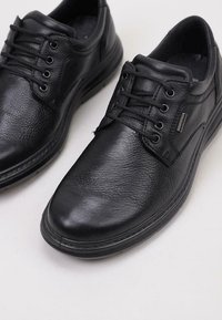Zapatos de cuero negro con punta redondeada, superficie texturizada y seis ojales. Cuentan con un acolchado en el collar y suela de goma plana.