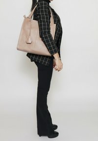 Lichtroze leren tote bag met een hexagonale accent, gestructureerd oppervlak en stevige banden. Gedragen met een zwart geruit blazer en broek.