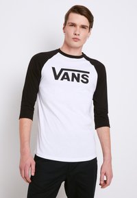 Sort og hvid raglan t-shirt med trekvart ærmer. Stort "VANS" logo i sort på den hvide front. Glat bomuldsstof.