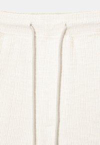 Shorts de sport texturés blancs avec un cordon de serrage à la taille, mettant en avant un accent gris. Le matériau semble doux et légèrement côtelé.